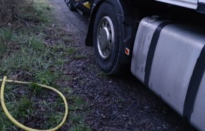 Na zdjęciu widać bak pojazdu ciężarowego i leżący obok  gumowy wąż